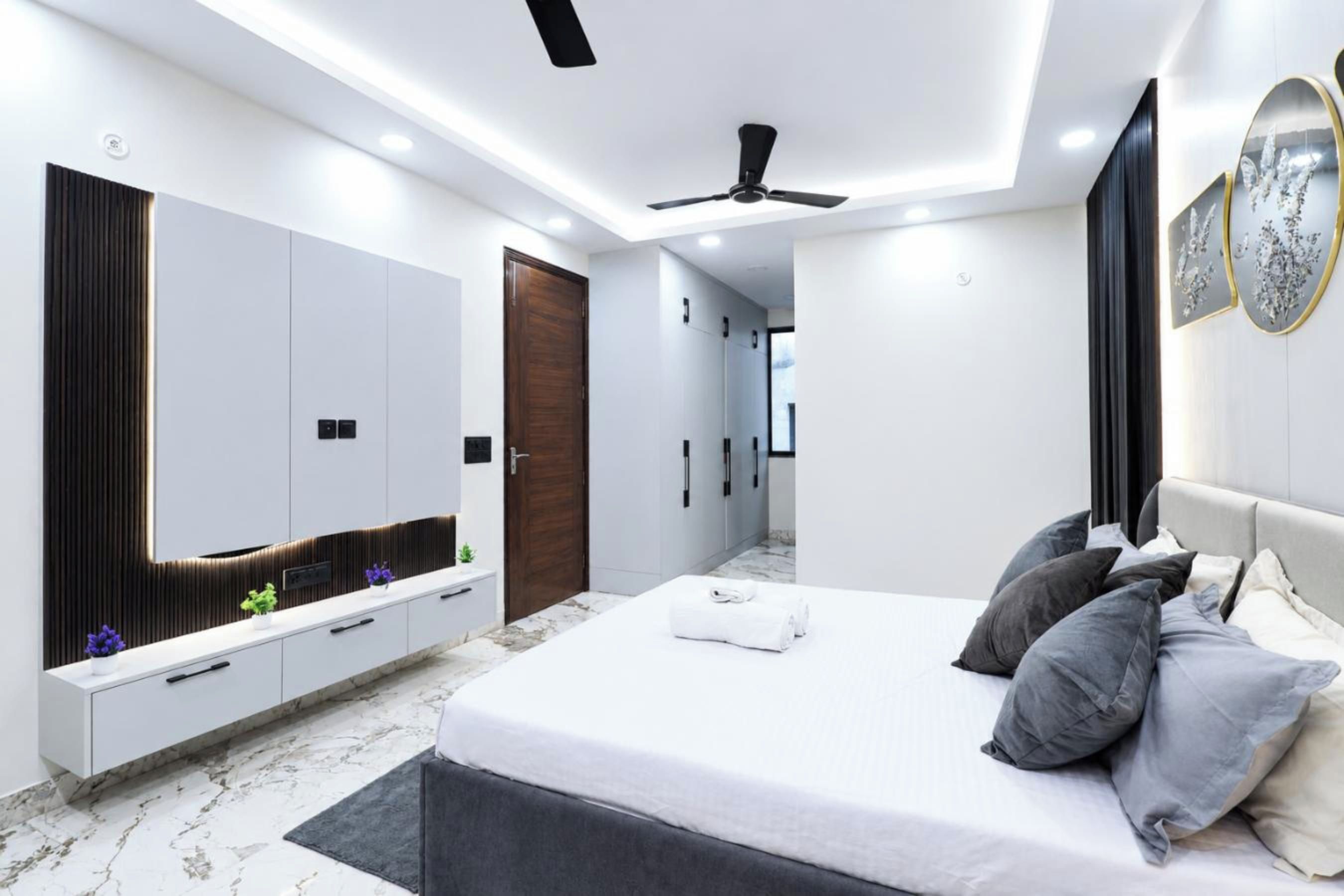 A modern bedroom with a large bed, a vanity with a mirror, and a ceiling fan.