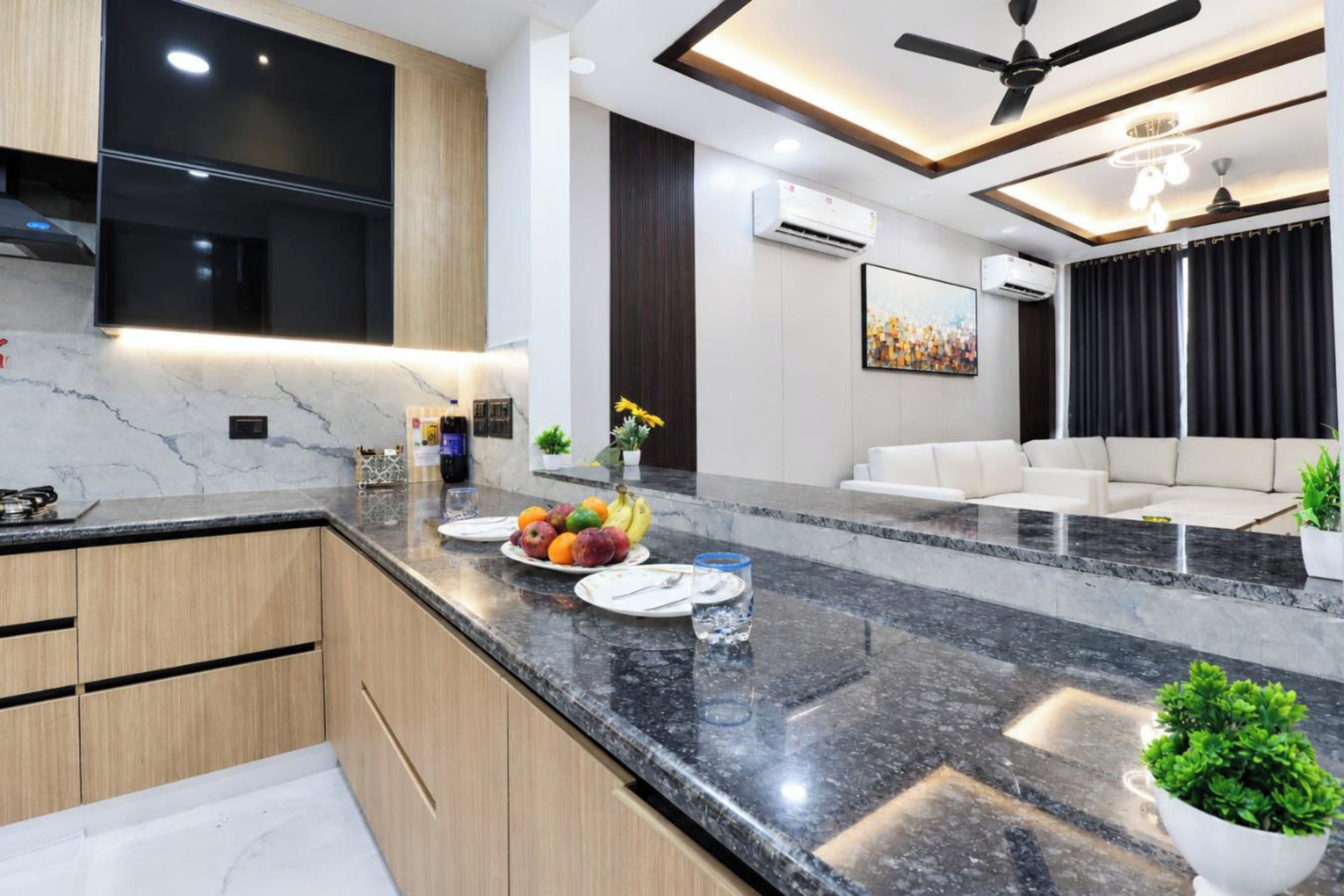 A modern kitchen with a marble countertop, wooden cabinets, and a dining area with a white sofa and a painting.