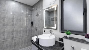 A modern bathroom with a large mirror, a white sink, and a shower.
