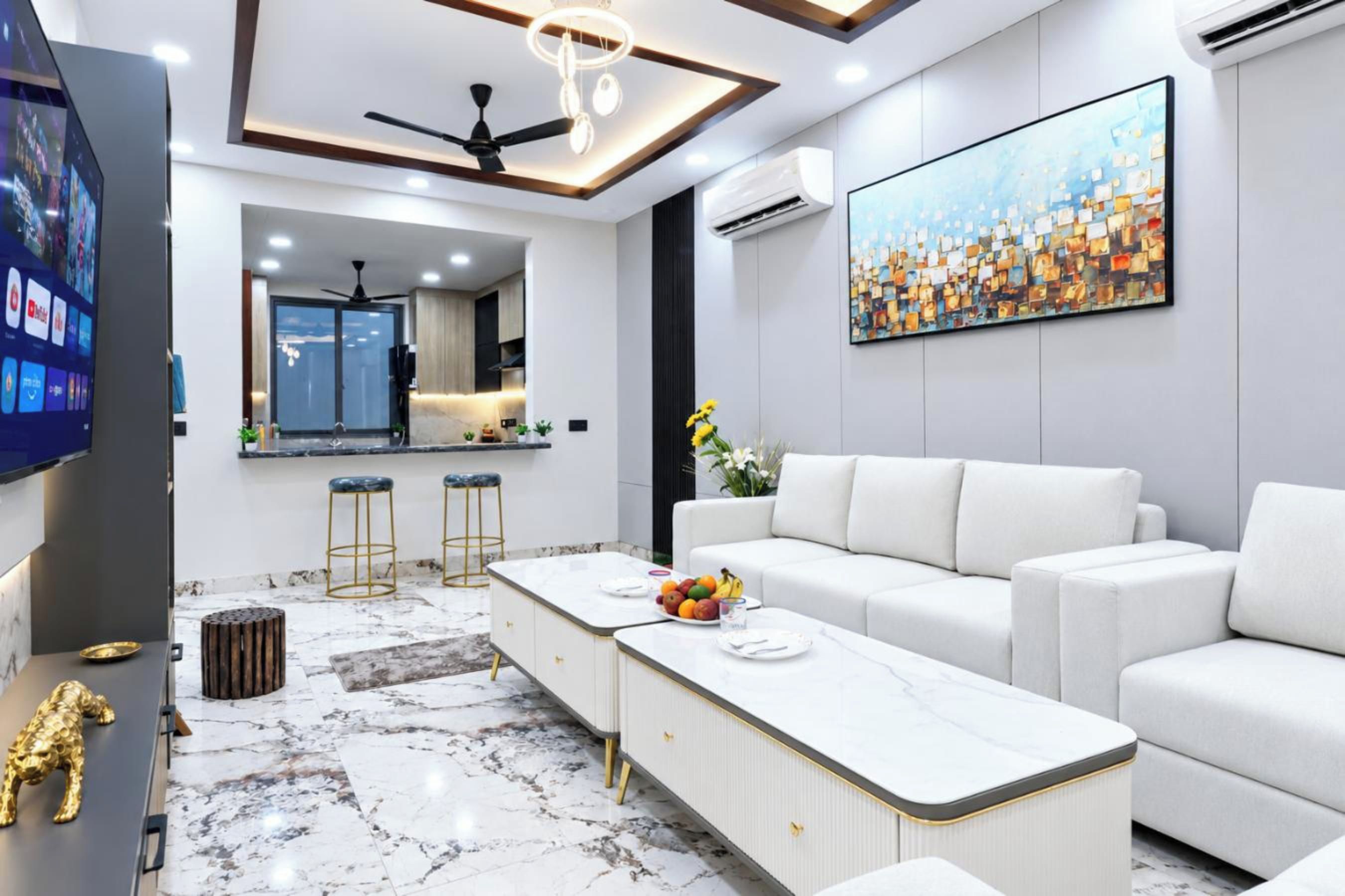 Uma sala de estar moderna com um sofá branco, piso de mármore, área de jantar com mesa branca e uma pintura grande na parede.