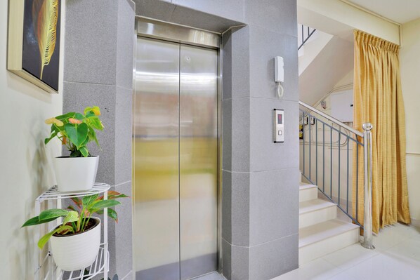 An elevator with a control panel, a staircase with a metal railing, and potted plants on a white shelf. - Super Collection O Lefort LUXE (Thiruvananthapuram)