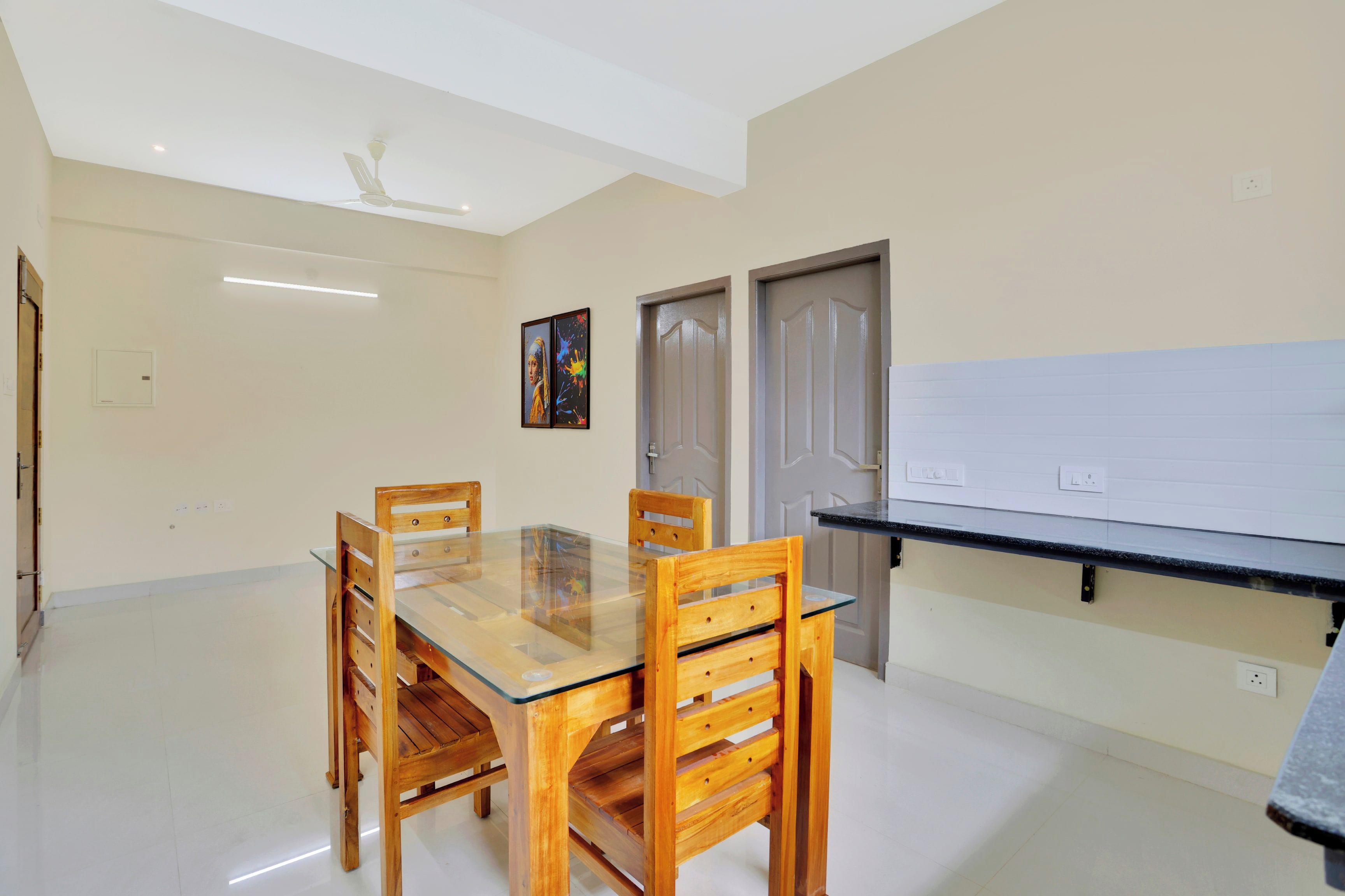 Un coin repas avec une table à plateau en verre et des chaises en bois, un ventilateur de plafond et une porte dotée d’une poignée.