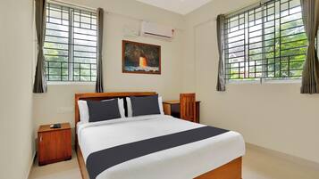 A hotel room with a bed, bedside tables, a painting, and windows with curtains.