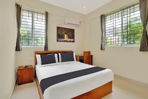 Una habitación de hotel con cama, mesitas de noche, un cuadro y ventanas con cortinas.