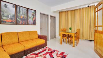 A living room with a sofa, a dining table with chairs, a rug, and a window with curtains.