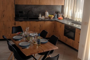 A modern kitchen with wooden cabinets, a black countertop, and a dining area with a wooden table set for four. - La Perla Vermentino Costa Paradiso Sardinia (Costa Paradiso)