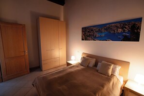 A bedroom with a bed, a wardrobe, a nightstand, a lamp, and a painting of a coastal landscape. - La Perla Vermentino Costa Paradiso Sardinia (Costa Paradiso)