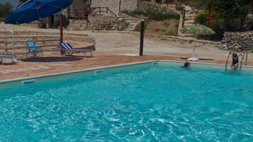 A swimming pool with lounge chairs and umbrellas, a stone building in the background, and a clear sky.