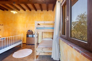 A room with a bunk bed, a small dresser, a window with a view, and a wooden ceiling.