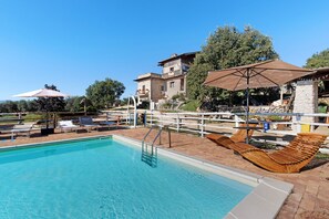 A pool area with lounge chairs, umbrellas, and a stone building in the background.