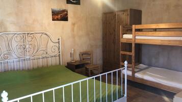 A room with a bunk bed, a single bed, a wooden wardrobe, a chair, and a small table.