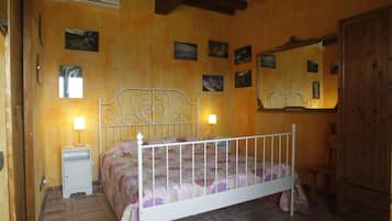 Ein Schlafzimmer mit einem Bettgestell aus weißem Metall, einem Nachttisch mit Lampe und einem Holzschrank.