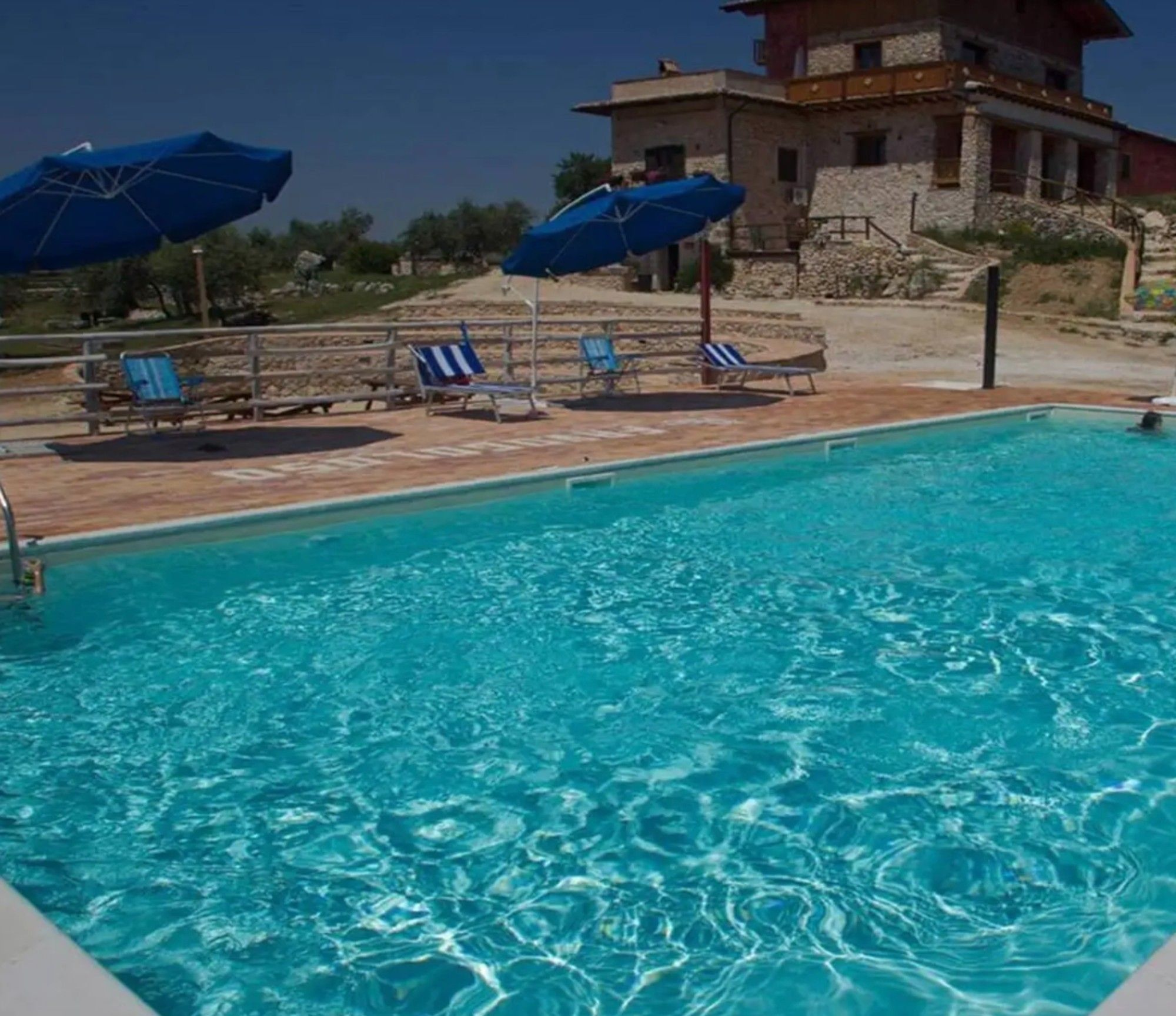 Una piscina con agua cristalina, rodeada de sillas de descanso y sombrillas azules.