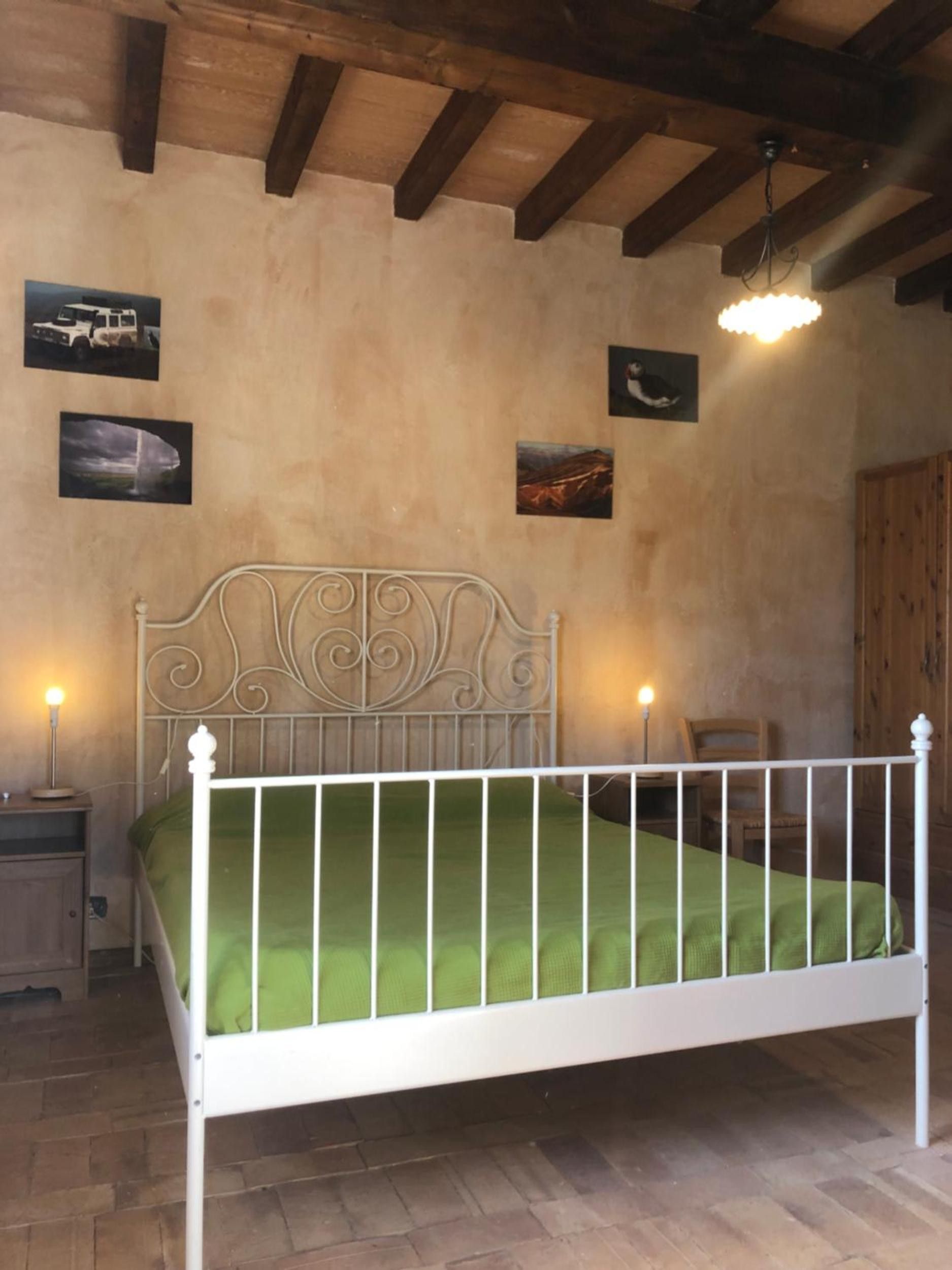 Ein Zimmer mit einem weißen Metallbett, grüner Bettwäsche, einer Holzzieldecke und einer Wand mit gerahmten Bildern.