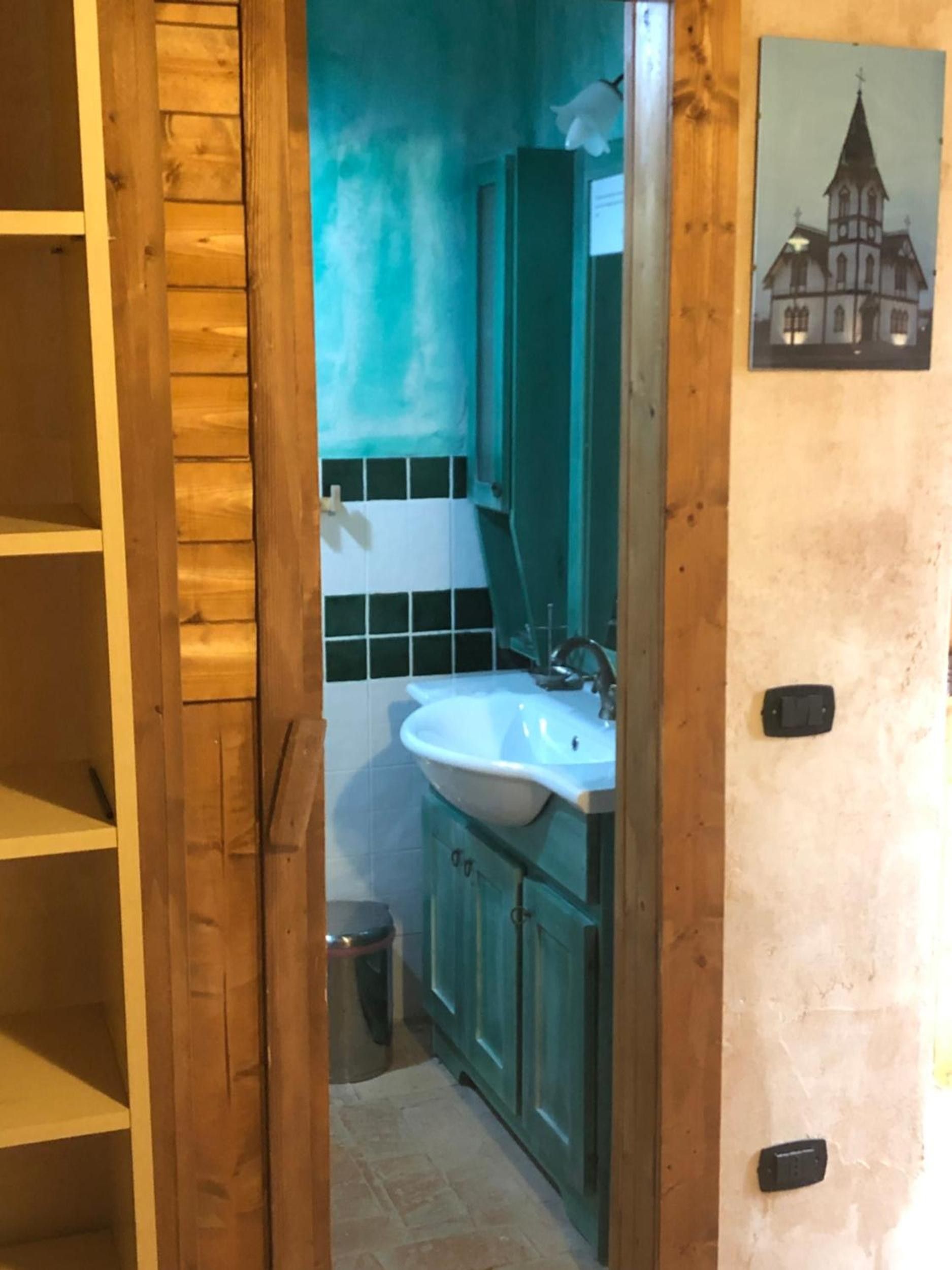 A bathroom with a wooden door, a sink, cabinets, and a trash bin.