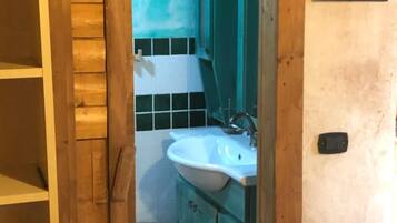 A bathroom with a wooden door, a sink, cabinets, and a trash bin.