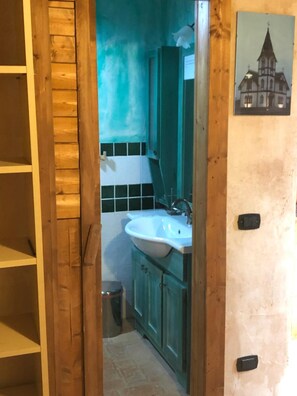Een badkamer met een houten deur, een wastafel, kastjes en een prullenbak.