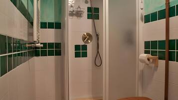 Un baño con cabina de ducha, inodoro y paredes con azulejos verdes.