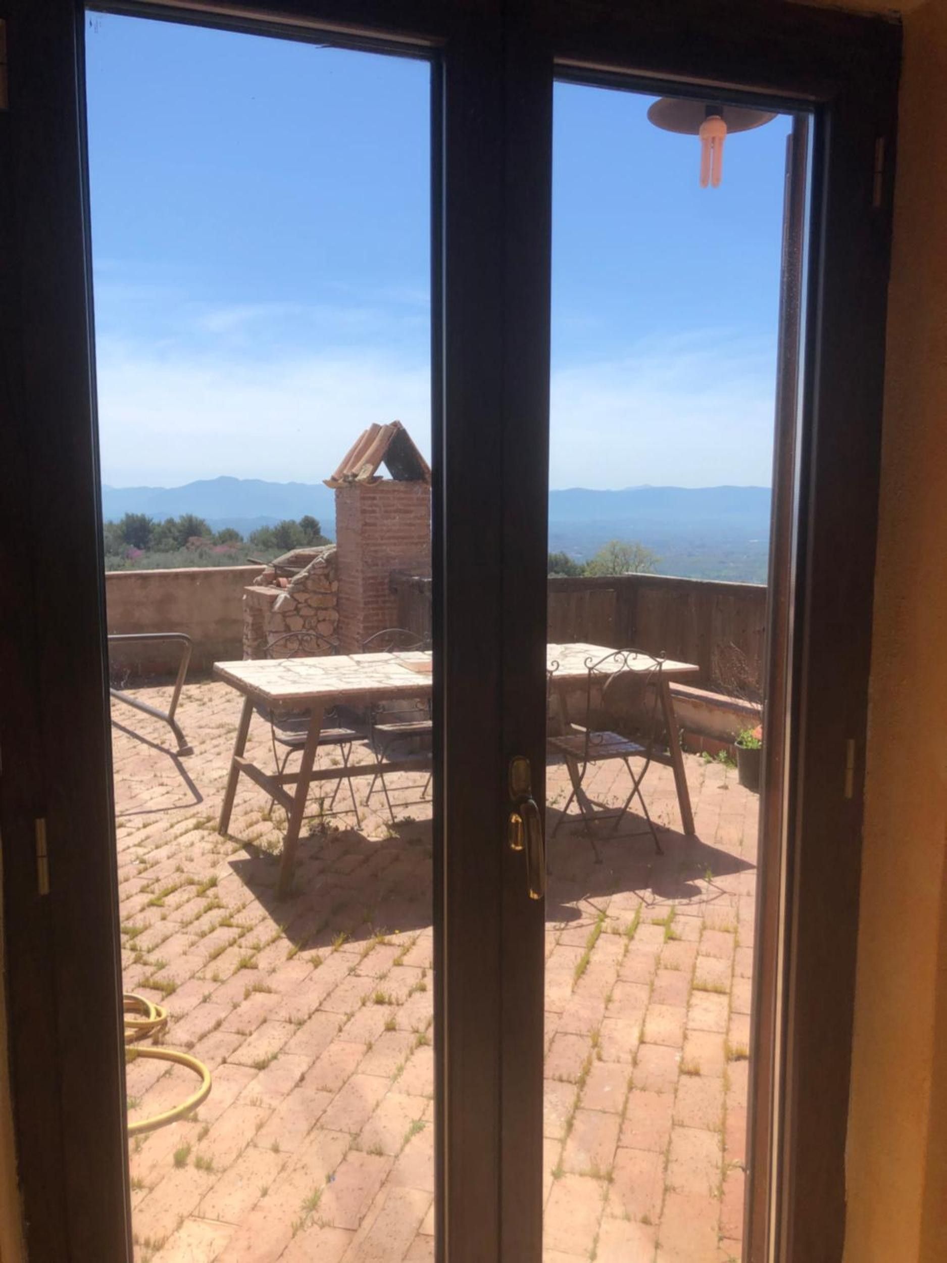 Eine Terrasse mit Tisch und Stühlen, ein Backsteinsschornstein und eine Aussicht auf ferne Berge.