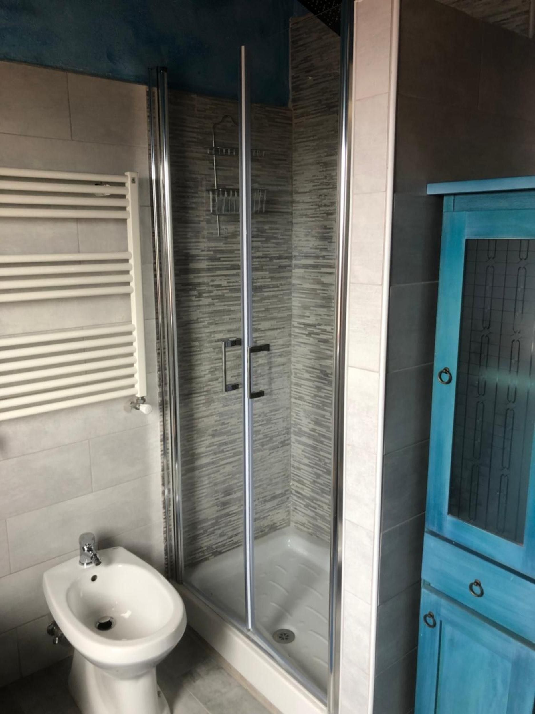 Ein Badezimmer mit einer gläsernen Duschkabine, einem weißen Waschbecken auf Säule und einem blauen Schrank.