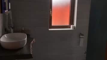 Un baño con un lavamanos blanco, una ventana con vidrio esmerilado y una alfombra azul en el suelo.