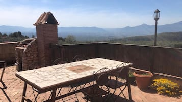 Un patio al aire libre con una mesa y sillas, un horno de ladrillo y vistas a montañas distantes.