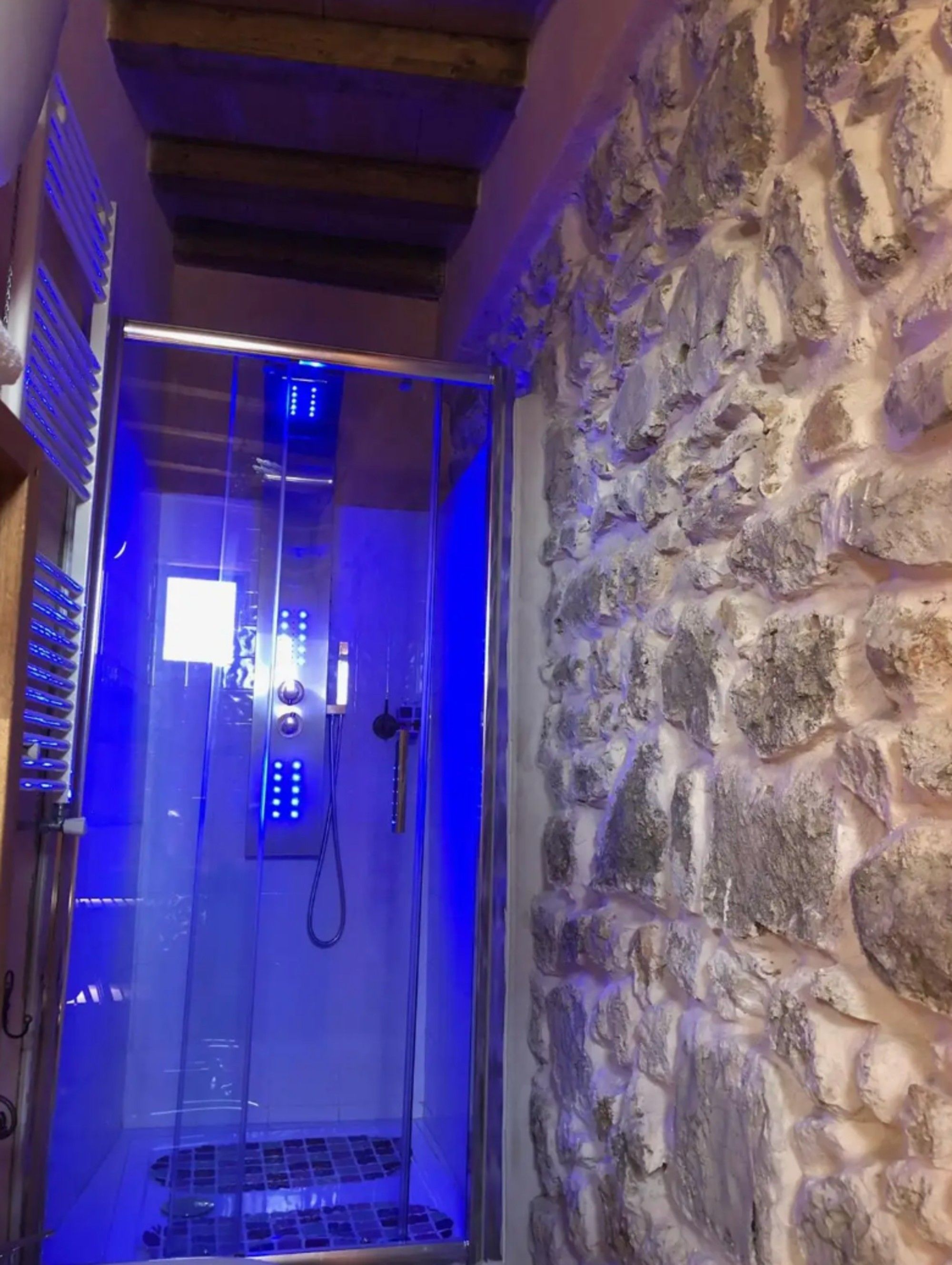 A glass-enclosed shower with a stone wall and wooden beams.