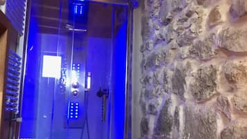 A glass-enclosed shower with a stone wall and wooden beams.