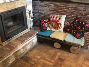 Un coin salon confortable avec un banc, des coussins et une cheminée.