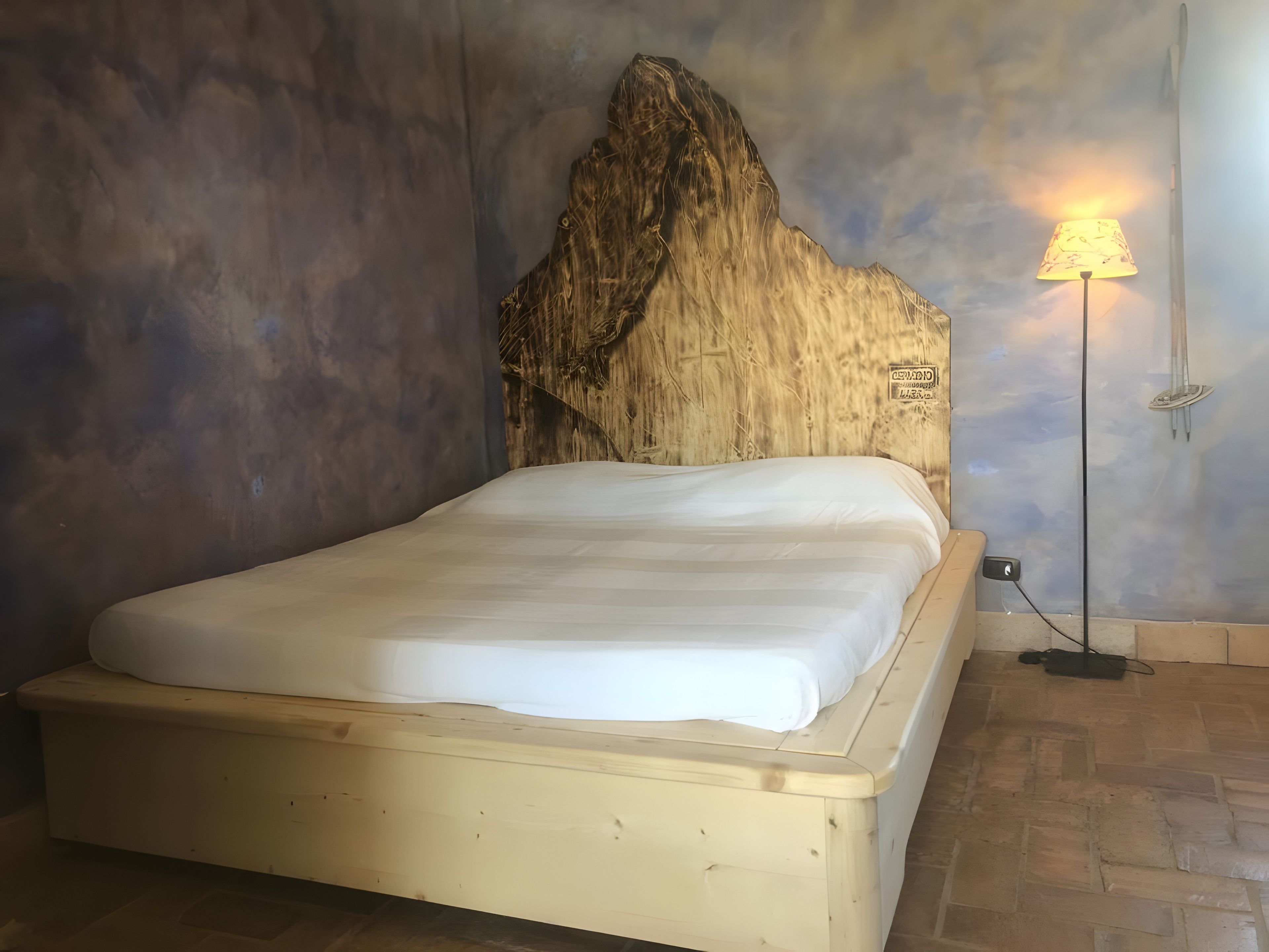 Ein Bett mit Holz-Kopfteil, einer Lampe und einer Wand mit Strukturputz.
