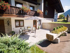 An outdoor patio with a wooden table and chairs, a potted plant, and a stone planter with flowers. - Dahoam Holiday Apartment at Schneidersepp with a terrace, bathroom with shower and toilet, Wi-Fi, max. 3 guests (Ruhpolding)