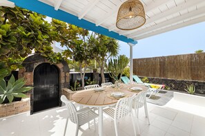 An outdoor patio with a round table set for dining, surrounded by white chairs, a black door, and a stone wall. - Paraiso Marino by Escape Home (Puerto del Carmen)