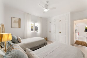 A bedroom with two beds, a ceiling fan, a window with curtains, and a wardrobe with multiple doors. - Paraiso Marino by Escape Home (Puerto del Carmen)