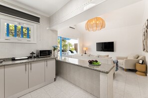 Una cuina moderna amb una illa central, una zona de menjador amb un sofà i un saló amb televisió.