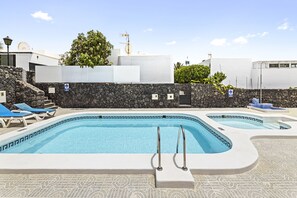 A swimming pool with two separate sections, a stone wall, and a few lounge chairs. - Paraiso Marino by Escape Home (Puerto del Carmen)