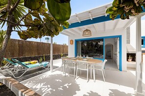A patio with a table and chairs, a covered seating area, and a view of the interior. - Paraiso Marino by Escape Home (Puerto del Carmen)