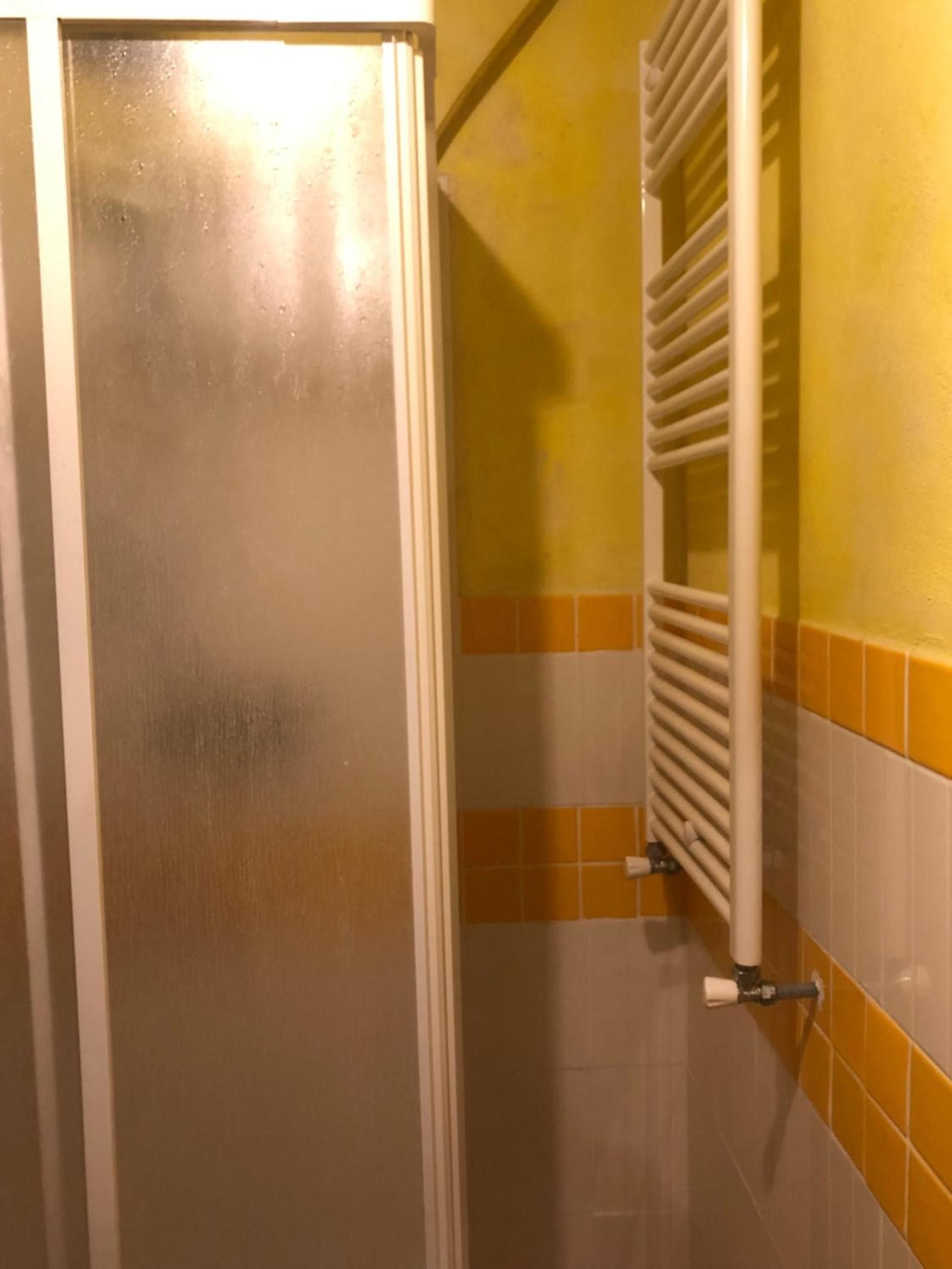 A bathroom with a white door, a white radiator, and yellow and white tiled walls.