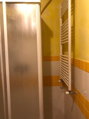Een badkamer met een witte deur, een witte radiator en wandtegels in geel en wit.