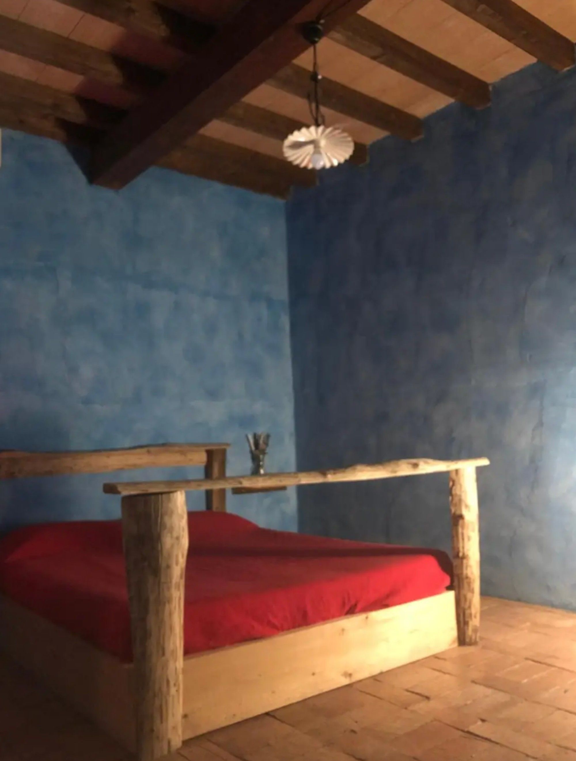 Ein Zimmer mit einem Bettgestell aus Holz, einer roten Matratze und einer Hängeleuchte.
