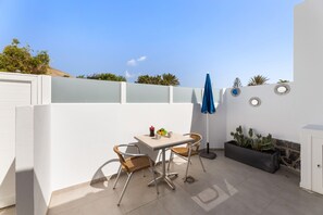 Un pati amb una taula i cadires, un para-sol blau, plats decoratius a la paret i una jardineria amb cactus.