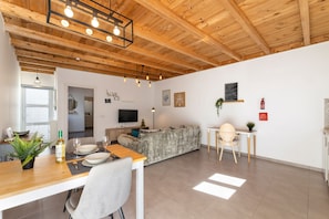 A modern living room with a wooden ceiling, a grey sofa, a dining table with chairs, a TV, and a fireplace. - Apartamento Alma 2 by Escape Home (Tías)