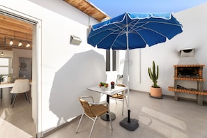 An outdoor patio with a table, chairs, a blue umbrella, a potted cactus, and a barbecue grill. - Apartamento Alma 2 by Escape Home (Tías)