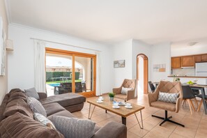 A modern living room with a sofa, armchairs, and a coffee table. There is a sliding glass door leading to a pool area. - Villa Conchita by Escape Home (Torre Solí Nou)