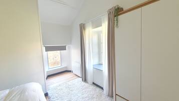 Quarto com janela, radiador, tapete branco e guarda-roupa.
