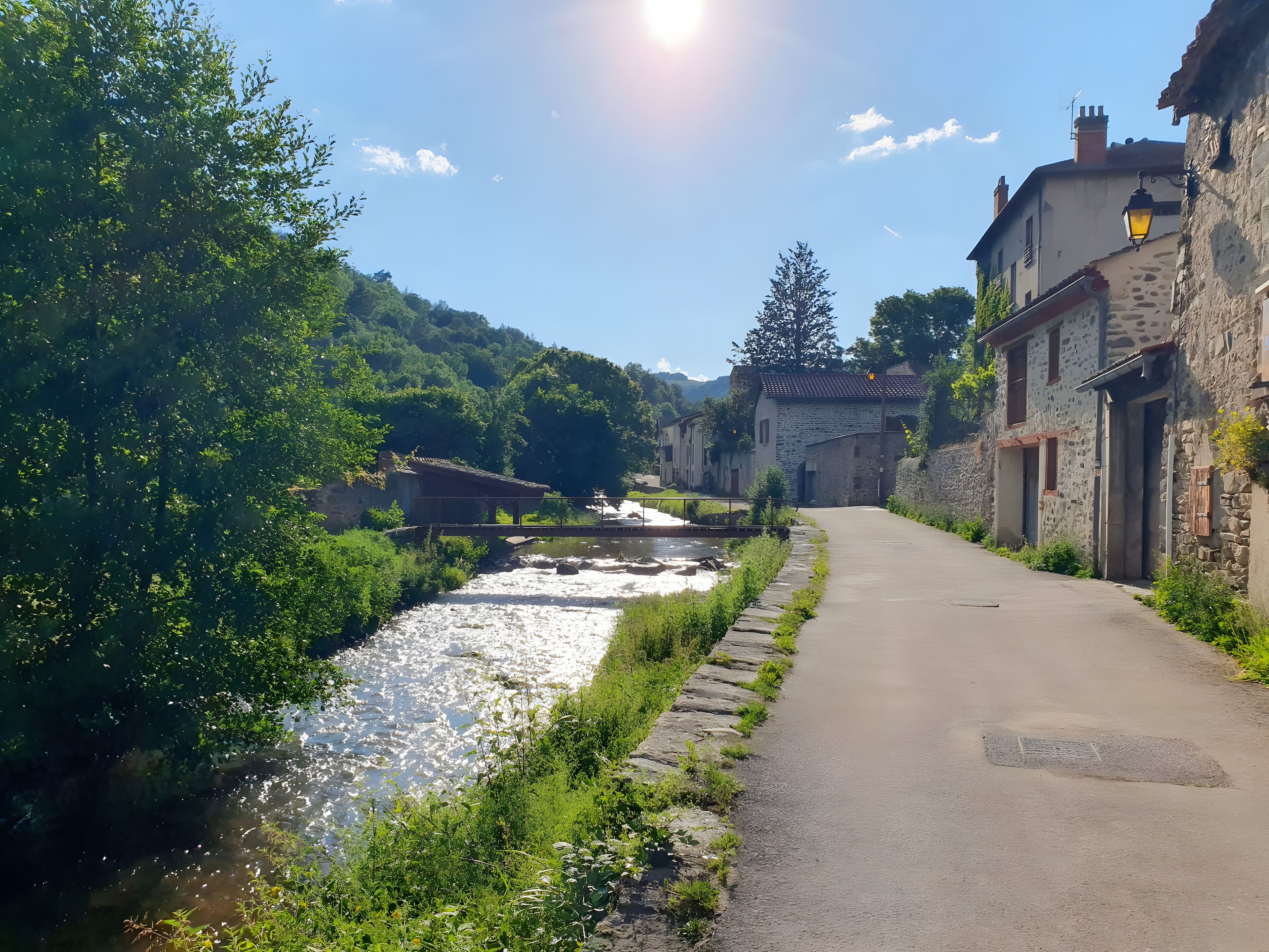 A narrow paved road flanked by stone buildings with a river running alongside.