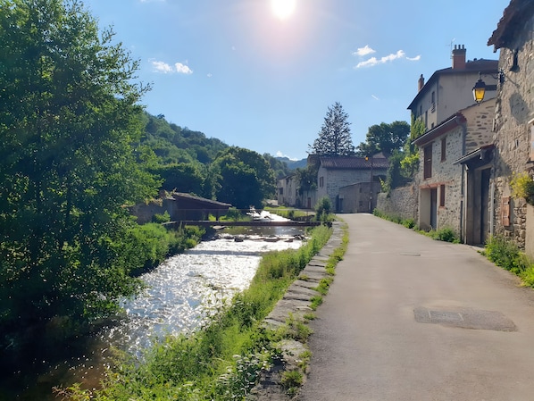 A narrow paved road flanked by stone buildings with a river running alongside.