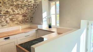 A kitchen with a stone wall, wooden countertop, white cabinets, and a window with a view. - Holiday Home 'Le Poulailler' with Private Garden, Summer Kitchen and Stunning Views (Blesle)