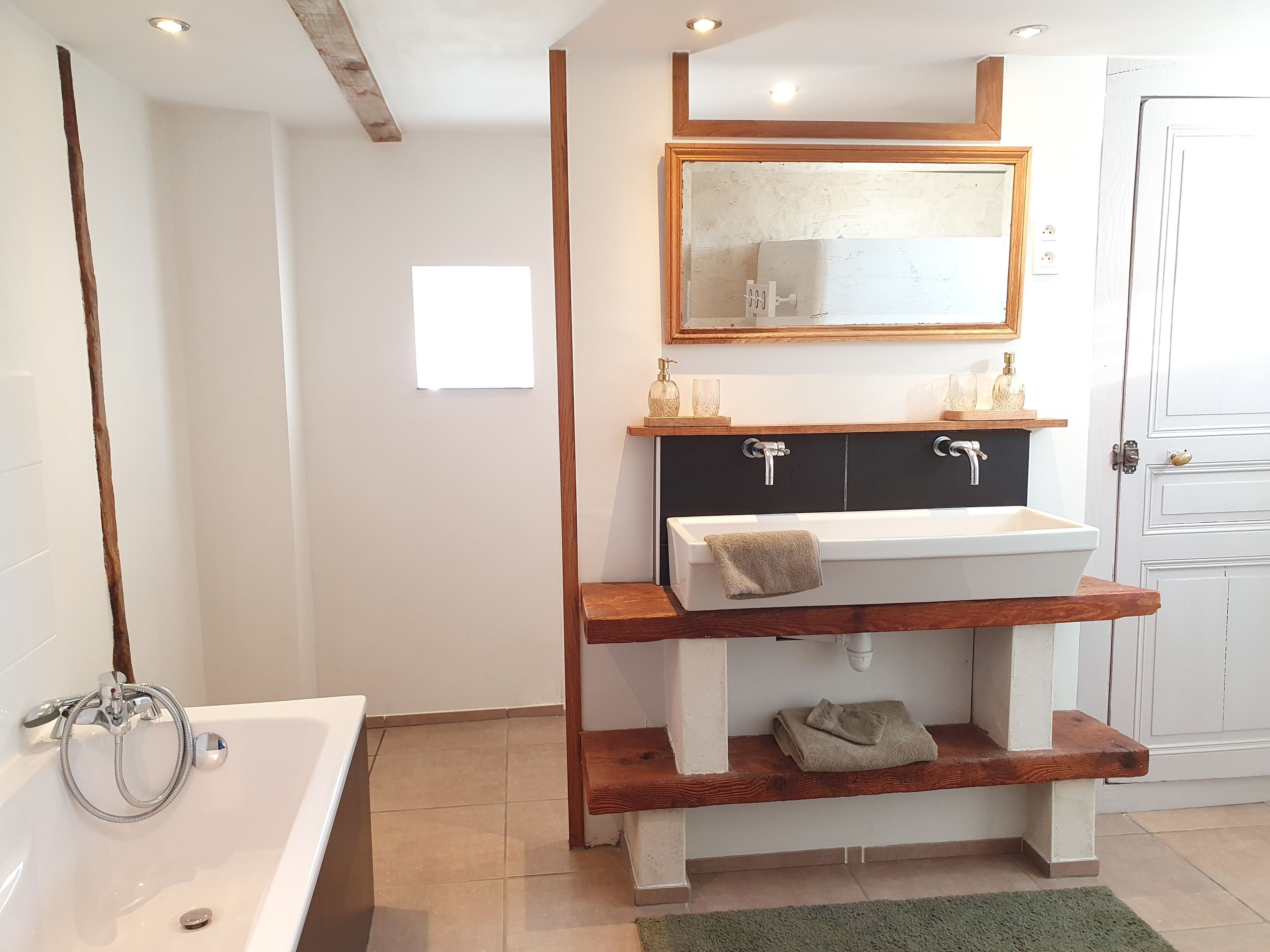 A bathroom with a white bathtub, a wooden vanity with a mirror, and a green rug.