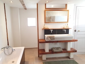 A bathroom with a white bathtub, a wooden vanity with a mirror, and a green rug. - Holiday Home 'Le Poulailler' with Private Garden, Summer Kitchen and Stunning Views (Blesle)