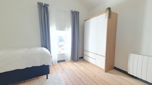 A bedroom with a bed, a wardrobe, a window with curtains, and a radiator. - Holiday Home 'Le Poulailler' with Private Garden, Summer Kitchen and Stunning Views (Blesle)